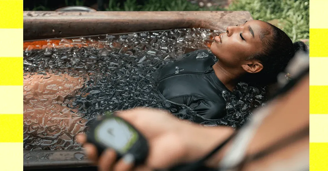 A person submerged in a cold plunge pool, shivering but determined, surrounded by ice and endurance-focused equipment.